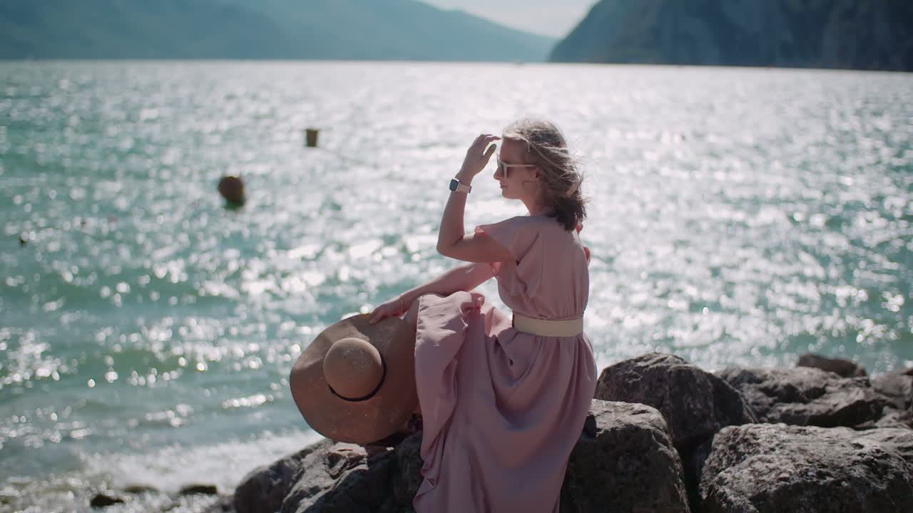 Woman Sitting on Rocky Seashore with Blue Sea Background