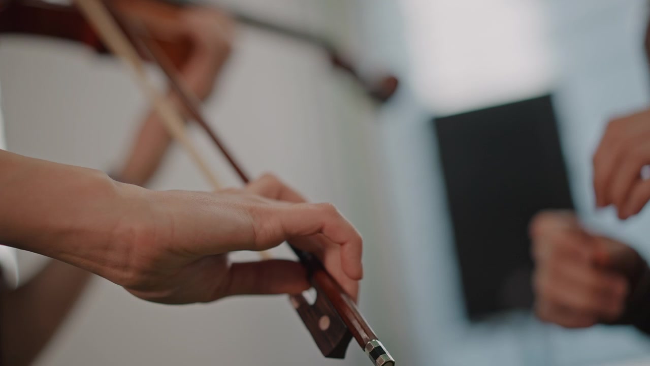 Teacher passing bow to student, gentle guidance captured in closeup hands, instructor correcting grip and balance, shared moment of trust in calm rehearsal room, patient coaching and technique