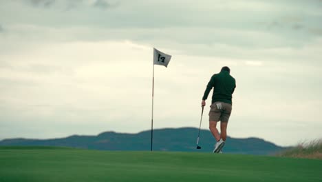 male golfer reading putting green, reading putt near pin with club in hand on ireland links golf course on beautiful sunny day, walking in slow motion