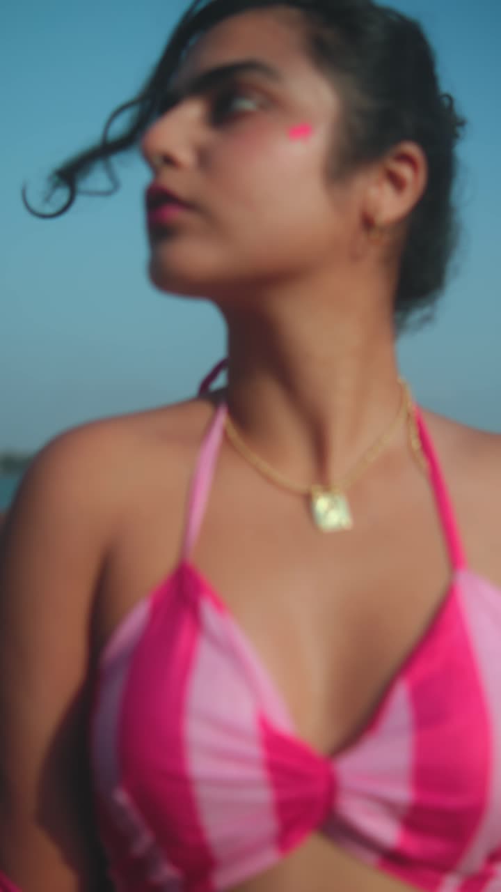 Giovane donna in bikini rosa a righe in spiaggia, che guarda in basso mentre si sistema il costume.
