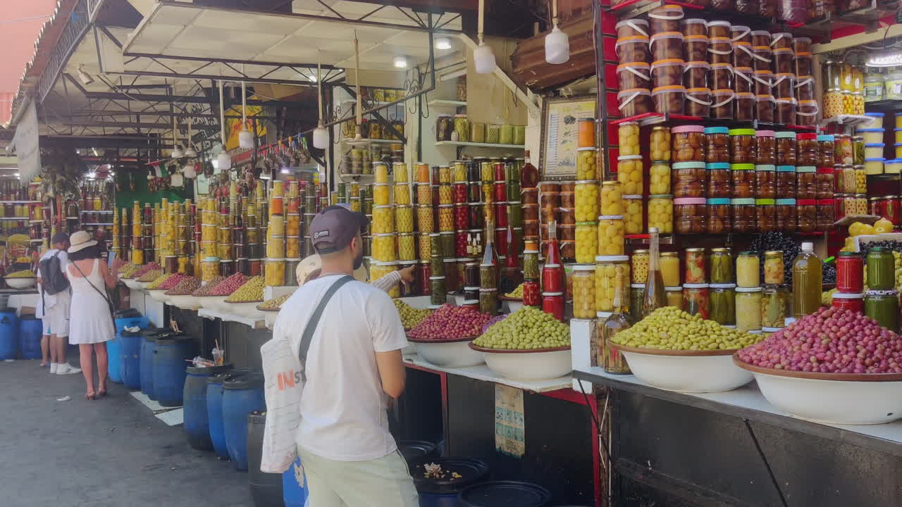 A bustling market in Marrakech with colorful jars of olives and spices on display under a canopy