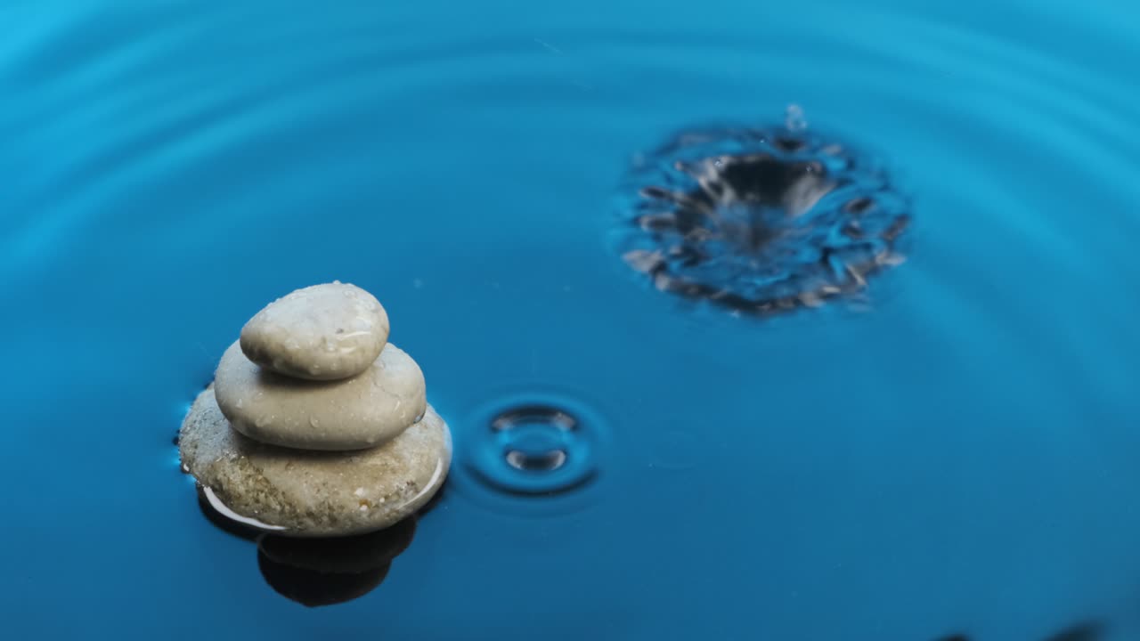 Falling drop of water into blue water with pyramid made of white stones.