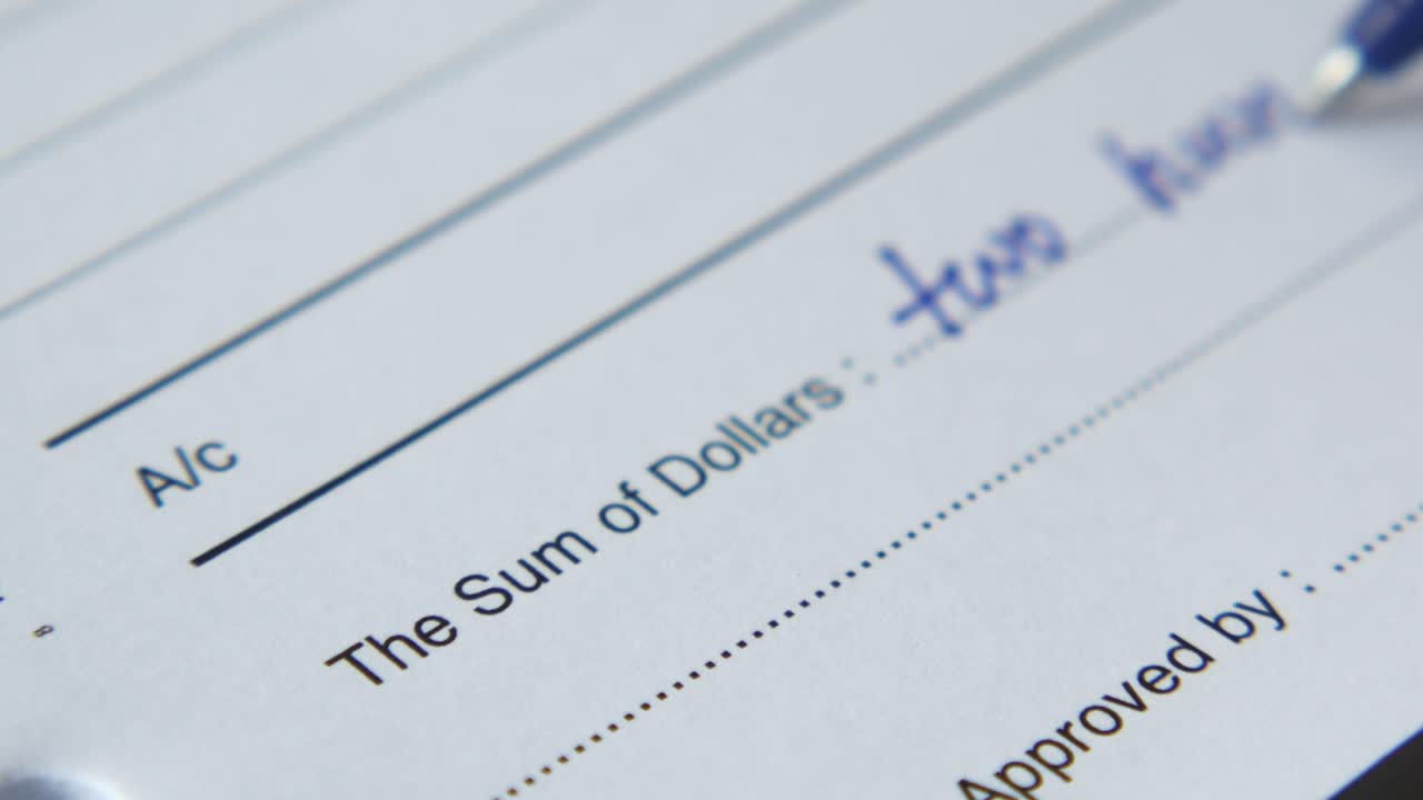 cerca de un cheque en blanco con un bolígrafo azul escribiendo la cantidad