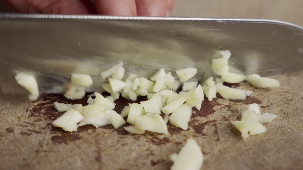 Close-up of Hands Chopping Garlic on a Wooden Cutting Board