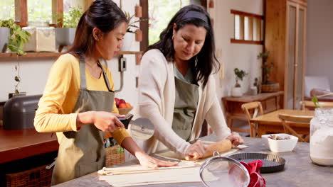 multiracial grandmother and young woman preparing pie dough together in cozy kitchen, at home