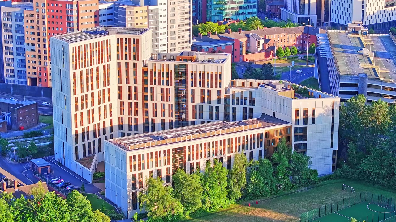 Urban skyline revealing modern apartment complexes surrounding green spaces, trees, and soccer field in Leeds city center during golden sunset lighting