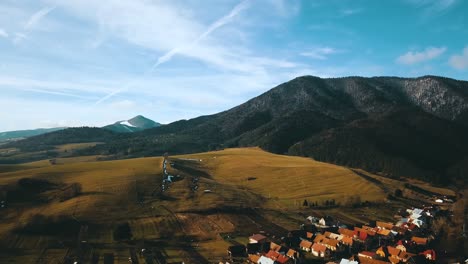 Drone-shot-over-village-with-mountain-above-it-and-blue-sky