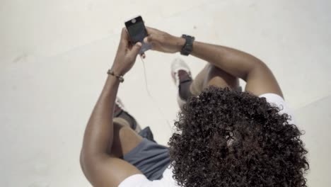 hombre afroamericano con teléfono inteligente sentado al aire libre.