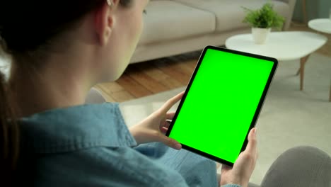 vista desde el hombro de la mujer sosteniendo y usando gestos de la mano en una pantalla de maqueta verde computadora tableta digital sentada en una silla. niña comprando cosas o navegando por internet