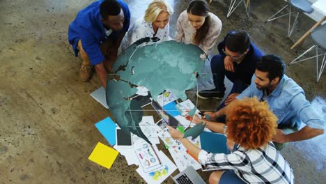 Animation-of-globe-rotating-over-diverse-creative-colleagues-brainstorming-on-office-floor