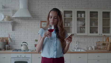 Attraktives-Mädchen,-Das-In-Der-Luxusküche-Ein-Mobiltelefon-Mit-Einem-Glas-Wein-Sucht.