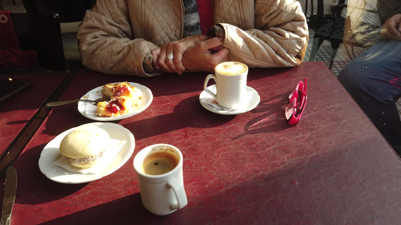 Patisserie coffee served in a french style restaurant table, hands close up with pedestrians passing by street