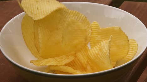 Wide-View-of-Potato-Chips-Crinkle-Cut-Crisps-Tumbling-into-White-Bowl-on-Picnic-Table-for-Party-in-Ultra-Slow-Motion---4K-Clip