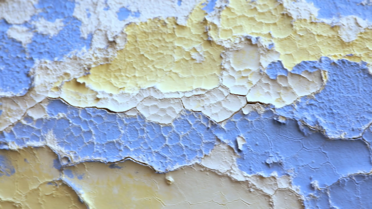 Closeup Peeling Paint Layers Showing Cracked Blue And Yellow Plaster Texture, Slow Pan Across Weathered Wall