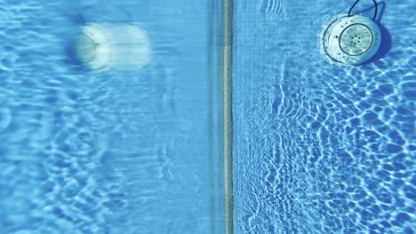 Cambio-De-Sillones-A-Bajo-El-Agua-De-Una-Piscina-Azul,-Tiro-Vertical