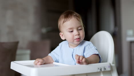 adorable caucasian toddler sitting at feeding table holding a bagel. cute kid plays with food dropping it on the floor.