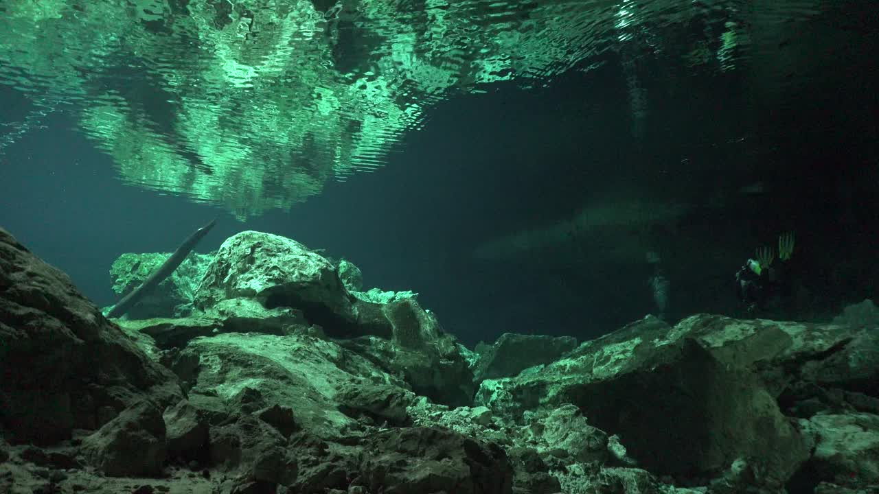 scuba diver llegando a la salida del sistema de cuevas cenotes tajma ha en yucatán méxico con formaciones rocosas que se reflejan en la superficie del agua