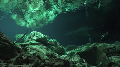 Scuba-Diver-Erreicht-Den-Ausgang-Des-Cenote-Höhlensystems-Tajma-Ha-In-Yucatan-Mexiko-Mit-Felsformationen,-Die-Sich-Auf-Der-Wasseroberfläche-Spiegeln