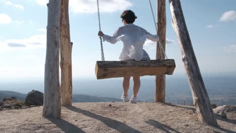 Back-view-of-woman-on-wooden-swing-enjoying-view-from-top-of-Folgosinho-mount