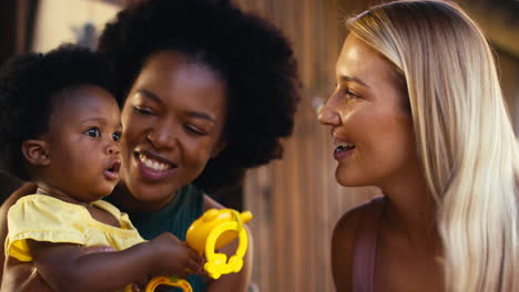 same sex family with two mums playing with young daughter and her toys  outdoors at home