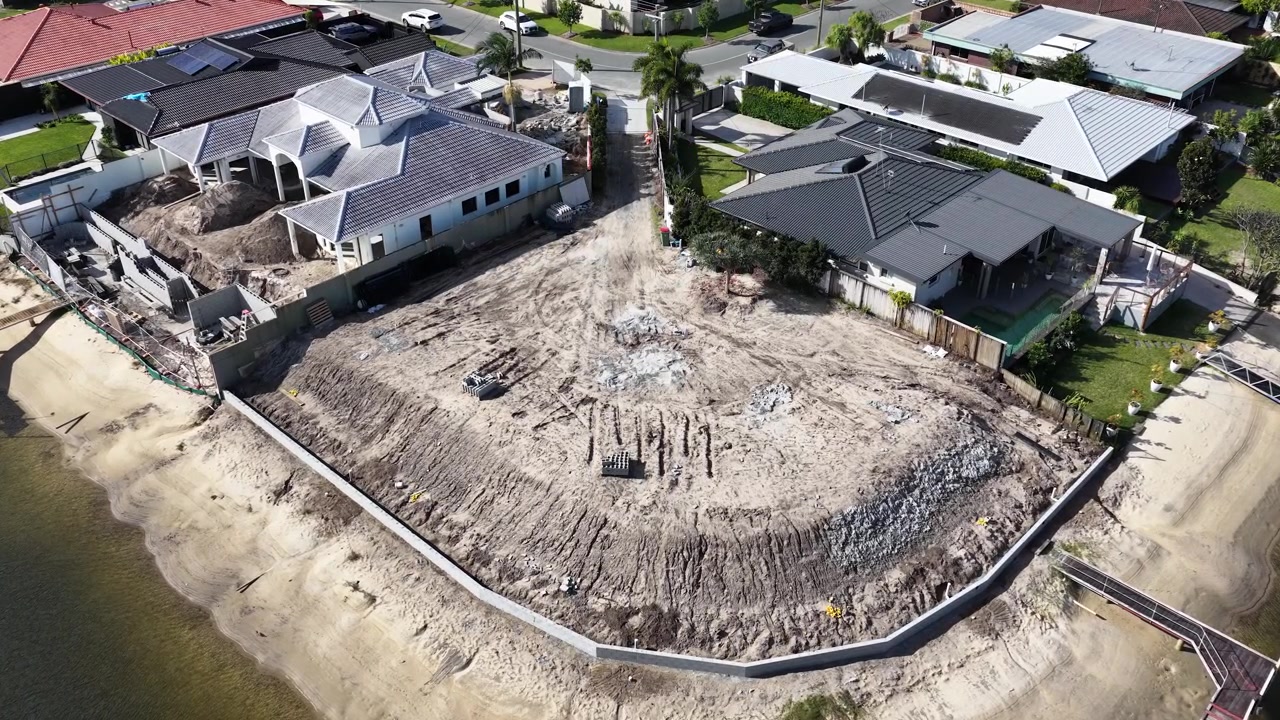 Drone shot reveals a vacant lot under development between luxury homes along a canal.