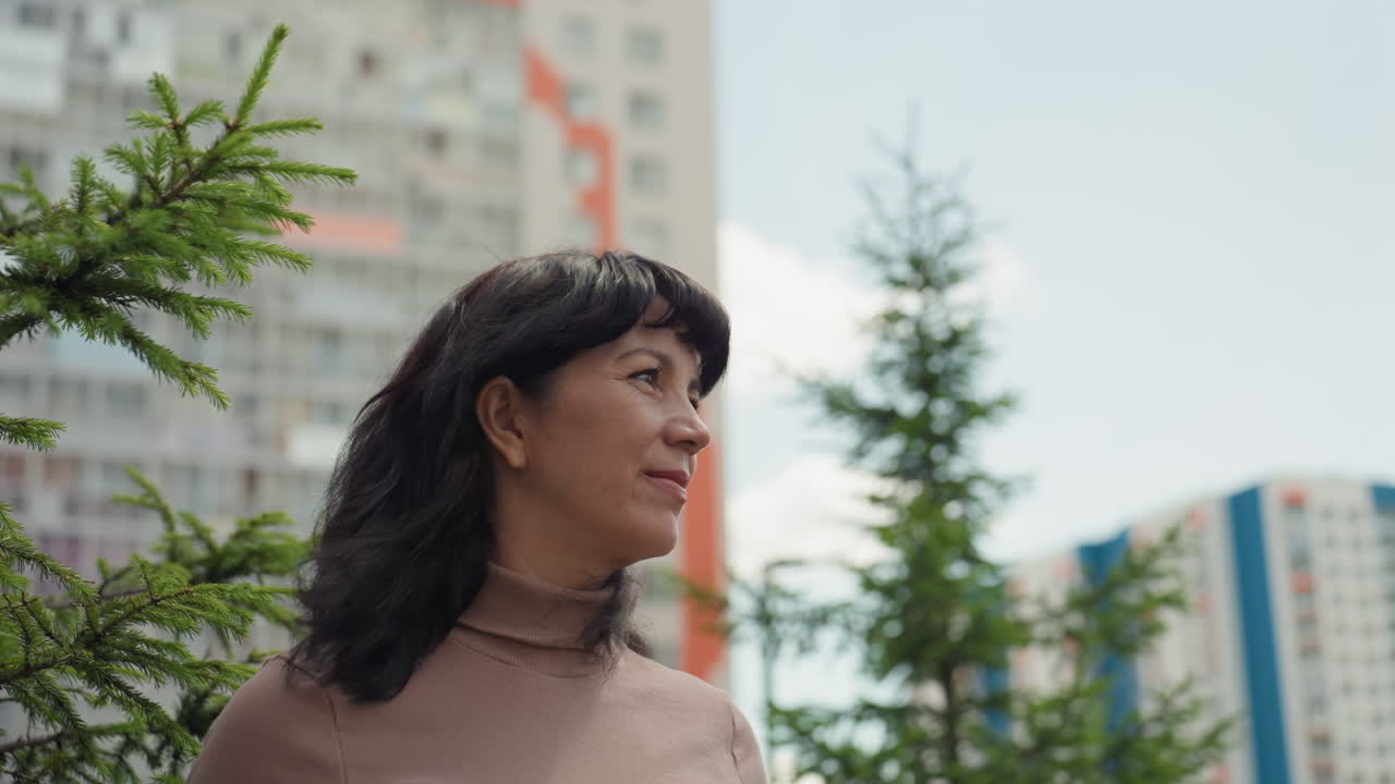 Caucasian Woman Contemplative Near Apartment Facade, Spruce Branch Framing Face, Soft Breeze, Thoughtful Expression, Creative Writer Energy, Urban Background With Colorful Mosaic Building