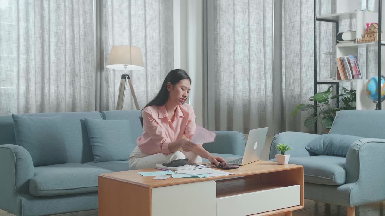노트북을 들고 있는 아시아 여성이 손에 든 청구서를 보고 머리를 흔들기 전에 지갑에 돈을 확인합니다.