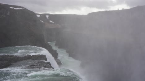 misty gullfoss waterfall in iceland with tourists on the edge, overcast weather