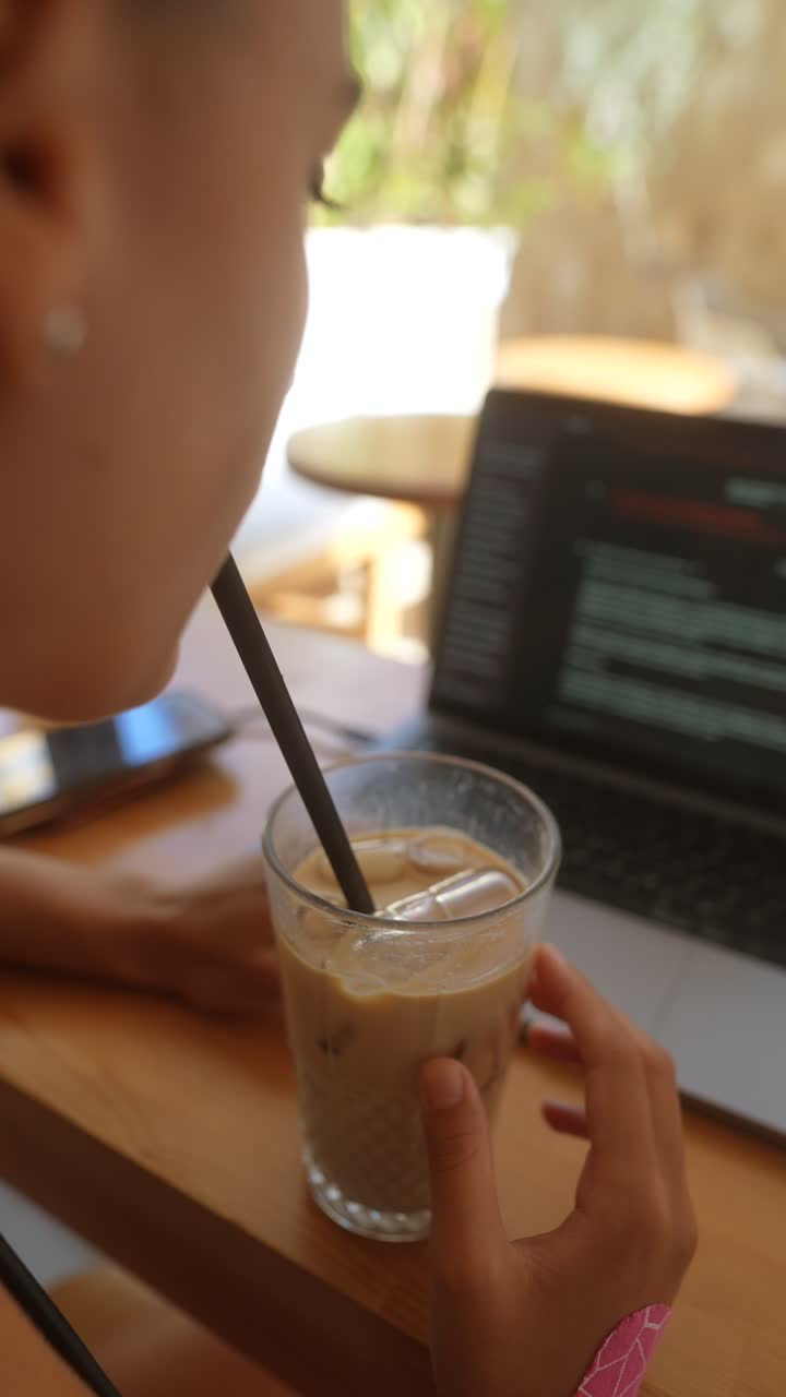 Donna che lavora al portatile in un bar con caffè freddo