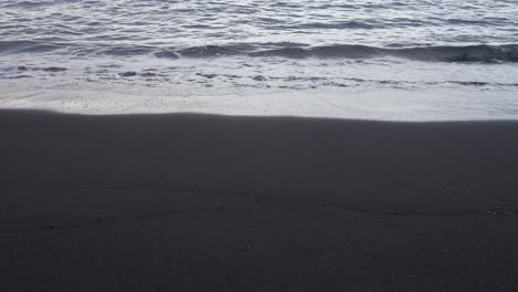 tenerife black volcanic sand beach with gentle waves lapping on the shore