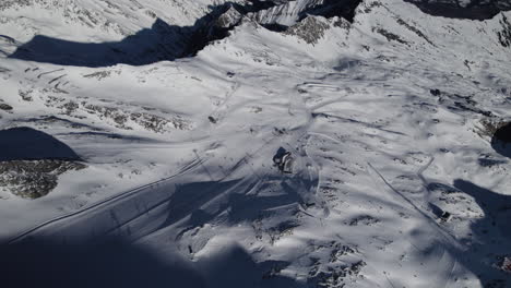 Aerial-top-down-shot-of-beautiful-snowy-mountain-slope-with-skiing-people-in-sun