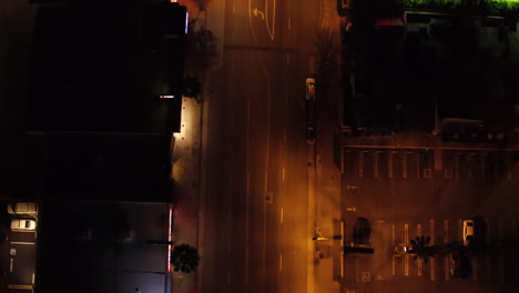 Toma-De-Arriba-Hacia-Abajo-De-La-Ciudad-Nocturna-Con-Un-Vehículo-De-Cuatro-Ruedas-Que-Pasa-Por-Un-Cruce-De-Carreteras