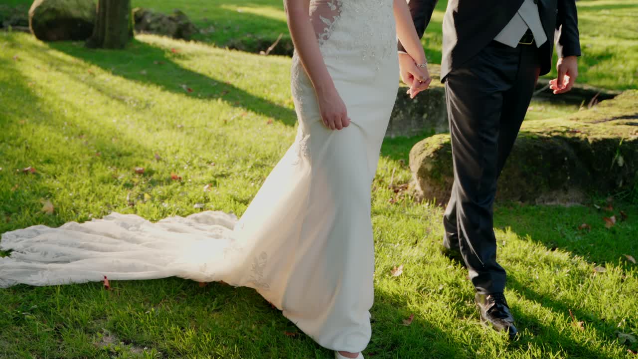 Bride and groom walking hand in hand on green grass in natural sunlight