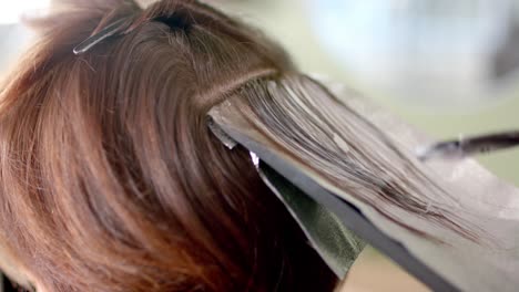 primer plano de la peluquera destacando el cabello del cliente con pincel y papel de aluminio en el salón de peluquería, en cámara lenta.