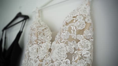 White-Wedding-Dress-With-Embroidered-Flower-Design-Next-To-Black-Bridesmaid-Dress-Hanging-On-The-Wall