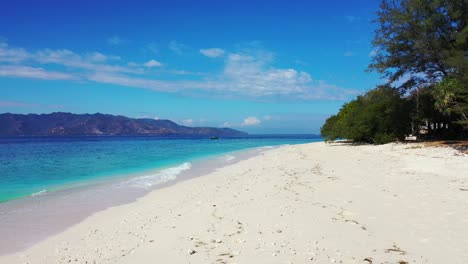 Tranquila-Playa-Exótica-Con-Arena-Blanca-Y-Guijarros-Bañados-Por-Olas-De-Mar-Azul-Celeste-Bajo-Un-Cielo-Azul-Brillante-Con-Nubes-Colgantes