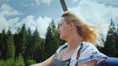 a young woman enjoys a lift on the lift looks at the beautiful mountains and forest around 4k video