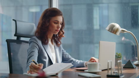 successful lady boss typing laptop checking information from notebook closeup.