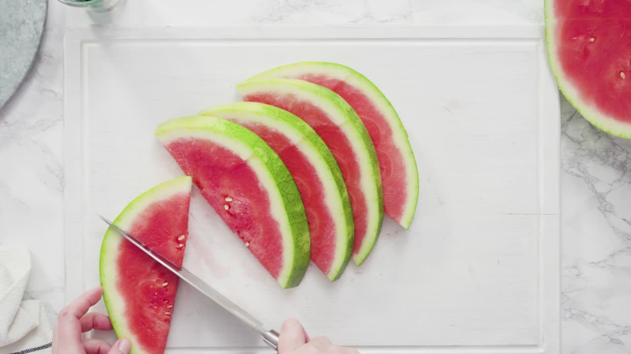 cortar la sandía roja en pedazos pequeños en una tabla de cortar blanca.