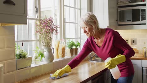 Feliz-Mujer-Caucásica-Mayor-Usando-Guantes-De-Goma,-Limpiando-Encimera-En-La-Cocina