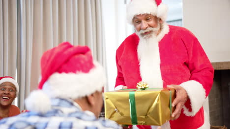 Happy-diverse-senior-friends-in-santa-outfit-and-christmas-hats-exchanging-gift-at-home,-slow-motion