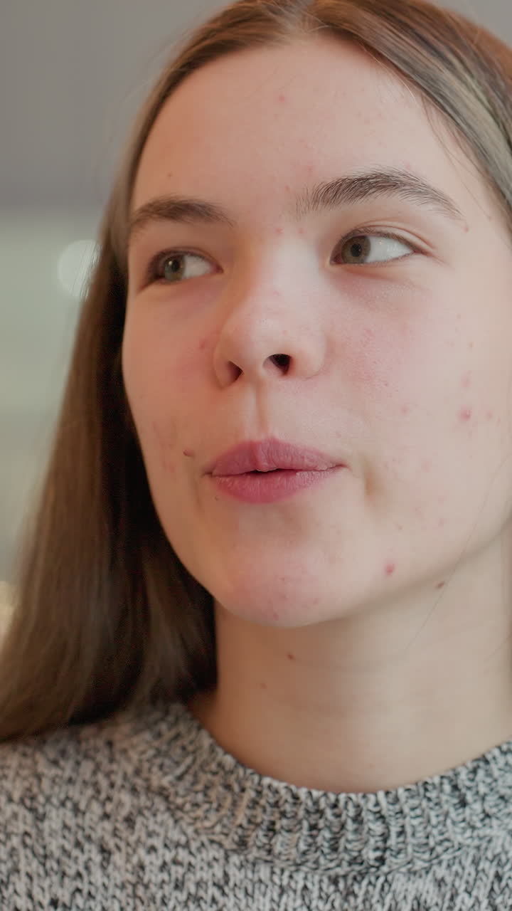 Primer plano de una joven caucásica probando una cucharada de yogur durante el desayuno matutino. El retrato muestra un gesto pensativo al masticar y una leve sonrisa, jersey de cocina cómodo, evaluando la textura como probadora de un blog de comida casera