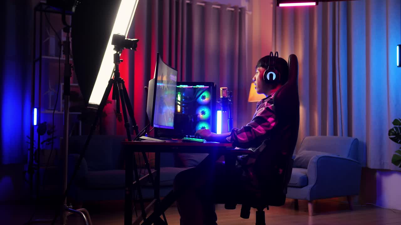 vista lateral de un niño asiático que juega a un juego en red en una computadora personal. desafío y amenaza de matanza de competidores, videojuego de transmisión en vivo, escritorio iluminado por luz de tira conducida por rgb