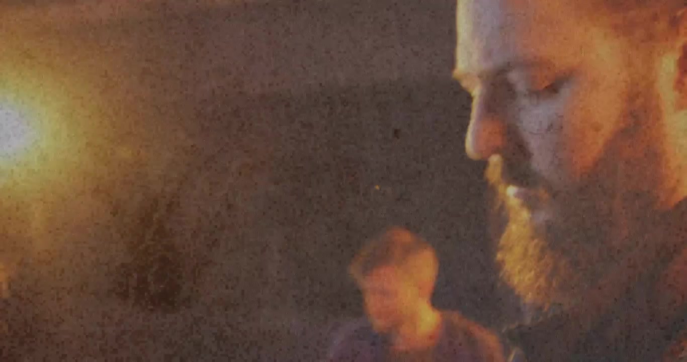 Chitarrista che impugna una paletta rossa, piroli mentre una lampada si accende, telecamera che mostra una prova musicale della band