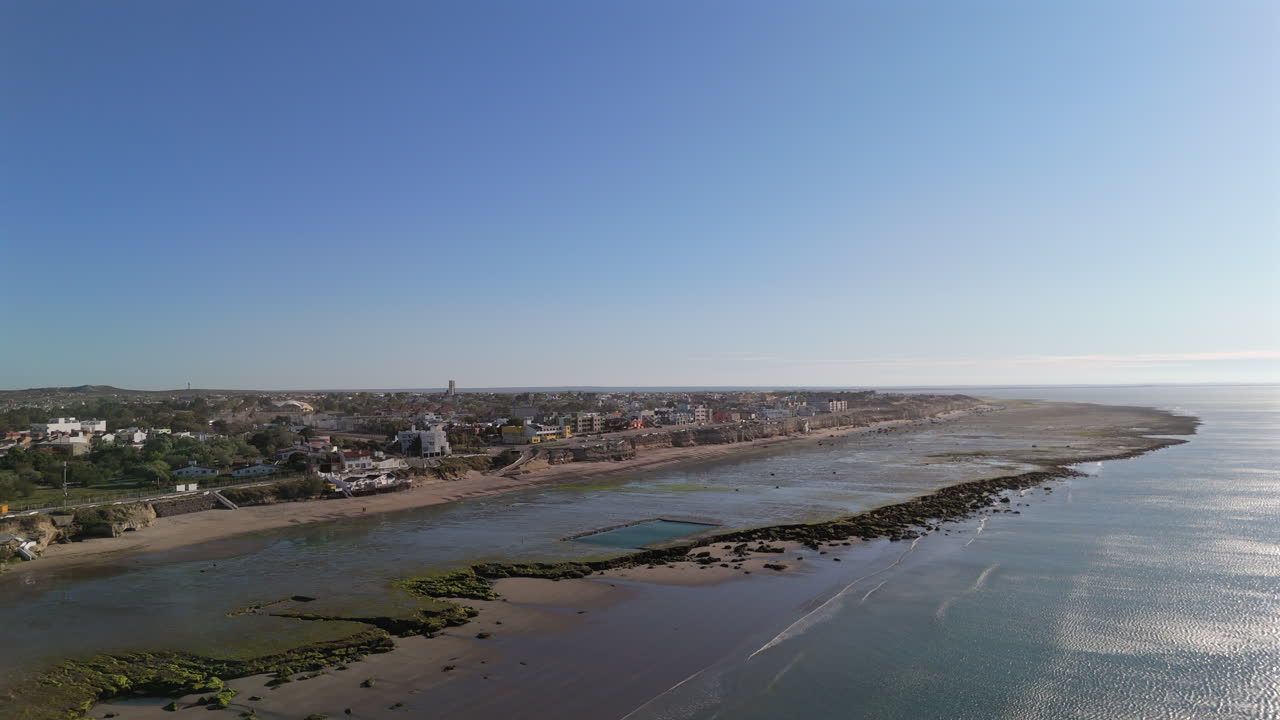 A panoramic view of Las Grutas beach, showcasing its beautiful shoreline at low tide. The calm waters stretch towards the horizon