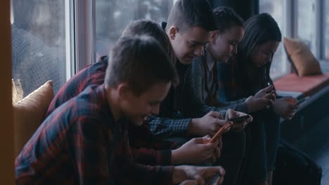 teenagers using smartphones by a window