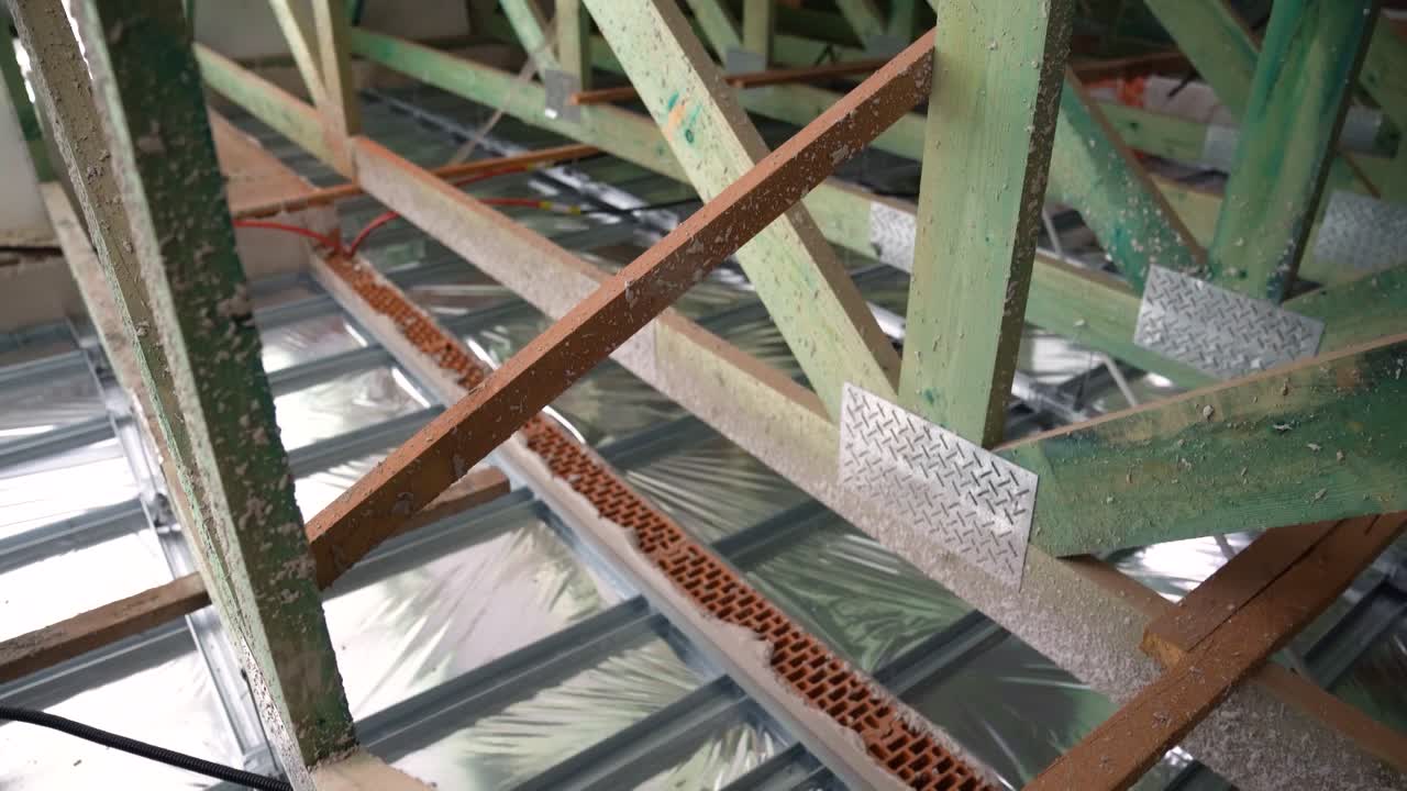 Cross-braced timber structure in attic with foil insulation and exposed bricks below