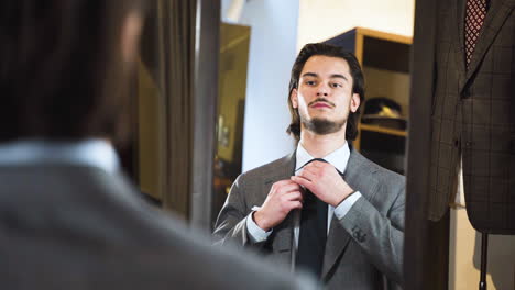 young bearded man trying on suit in front of fashion boutique mirror