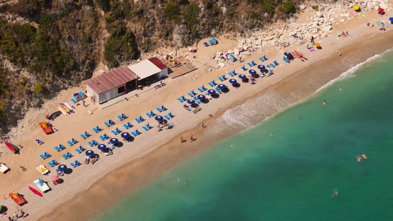 Birdview aerial drone shot of umbrellas and tourists enjoying Guidaloca Beach (Spiaggia di Guidaloca) in Scopello, Sicily, Italy, during sunny summer travel day