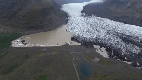 Aerial-view-getting-far-from-Svínafellsjökull-glacier,-with-different-ice-formations-and-focus-on-the-empty-roads-during-the-summer-of-Iceland